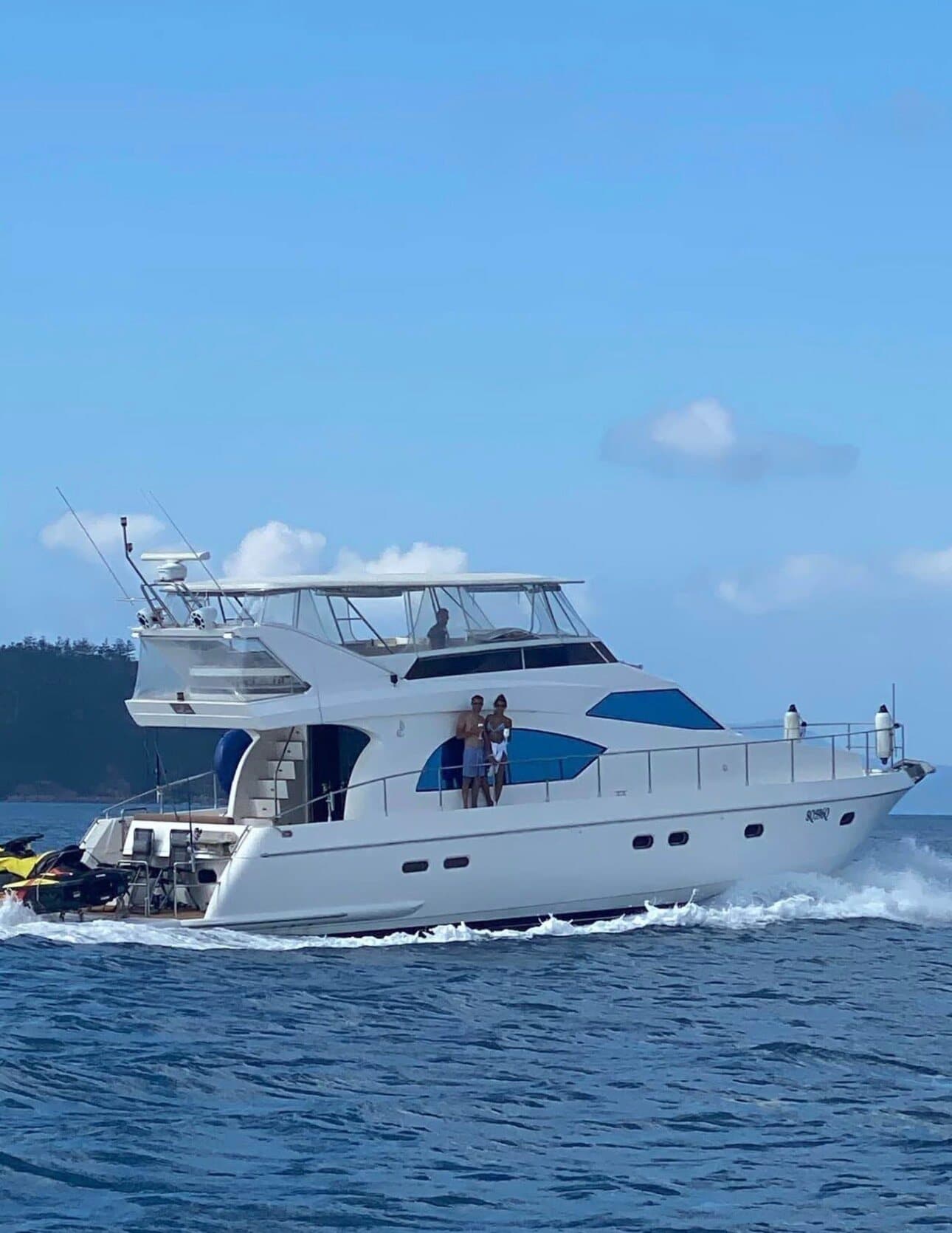 A white motor yacht cruising on blue water with jet skis on the stern
